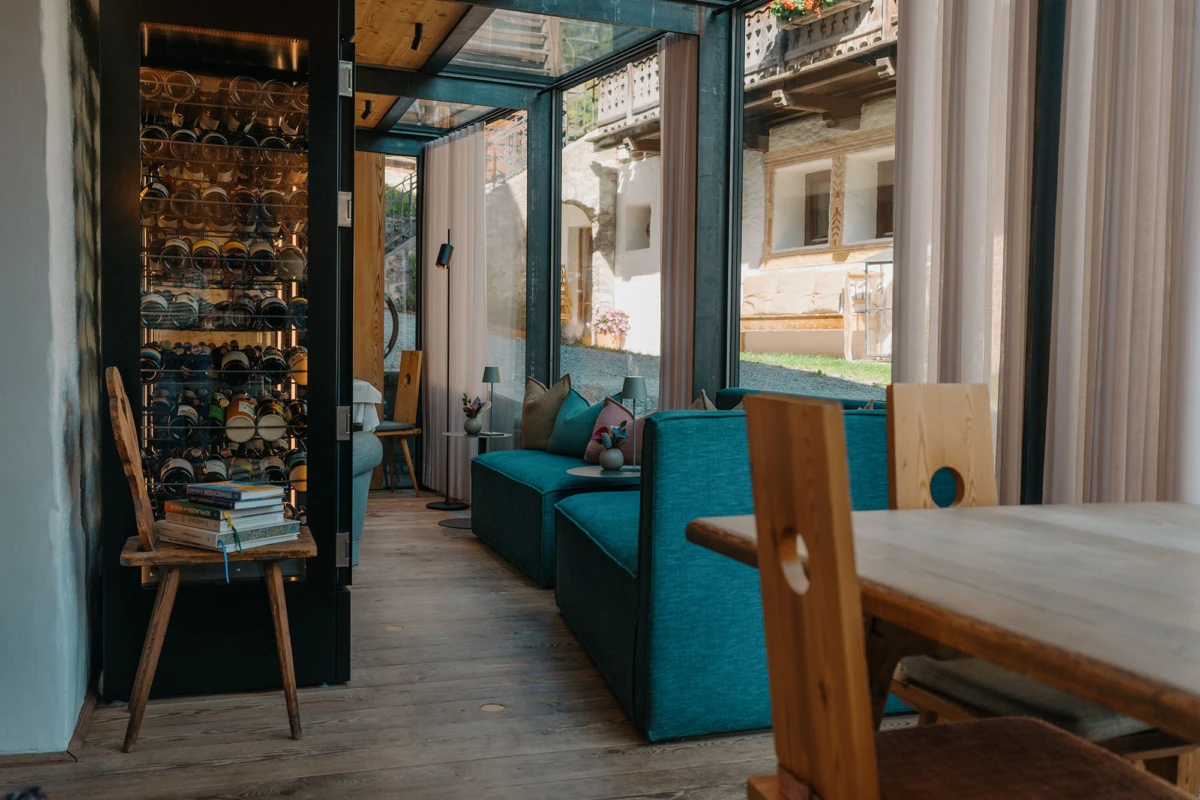 Wohnzimmer mit tealfarbenen Sofas, Esstisch und Stühle; links Weinregal, große Glasfronten mit Vorhängen.