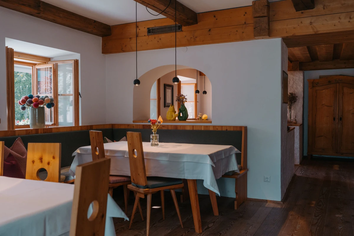 Gedeckter Esstisch im rustikalen Esszimmer mit Holzstühlen, weißen Tischdecken und Holzbalken.