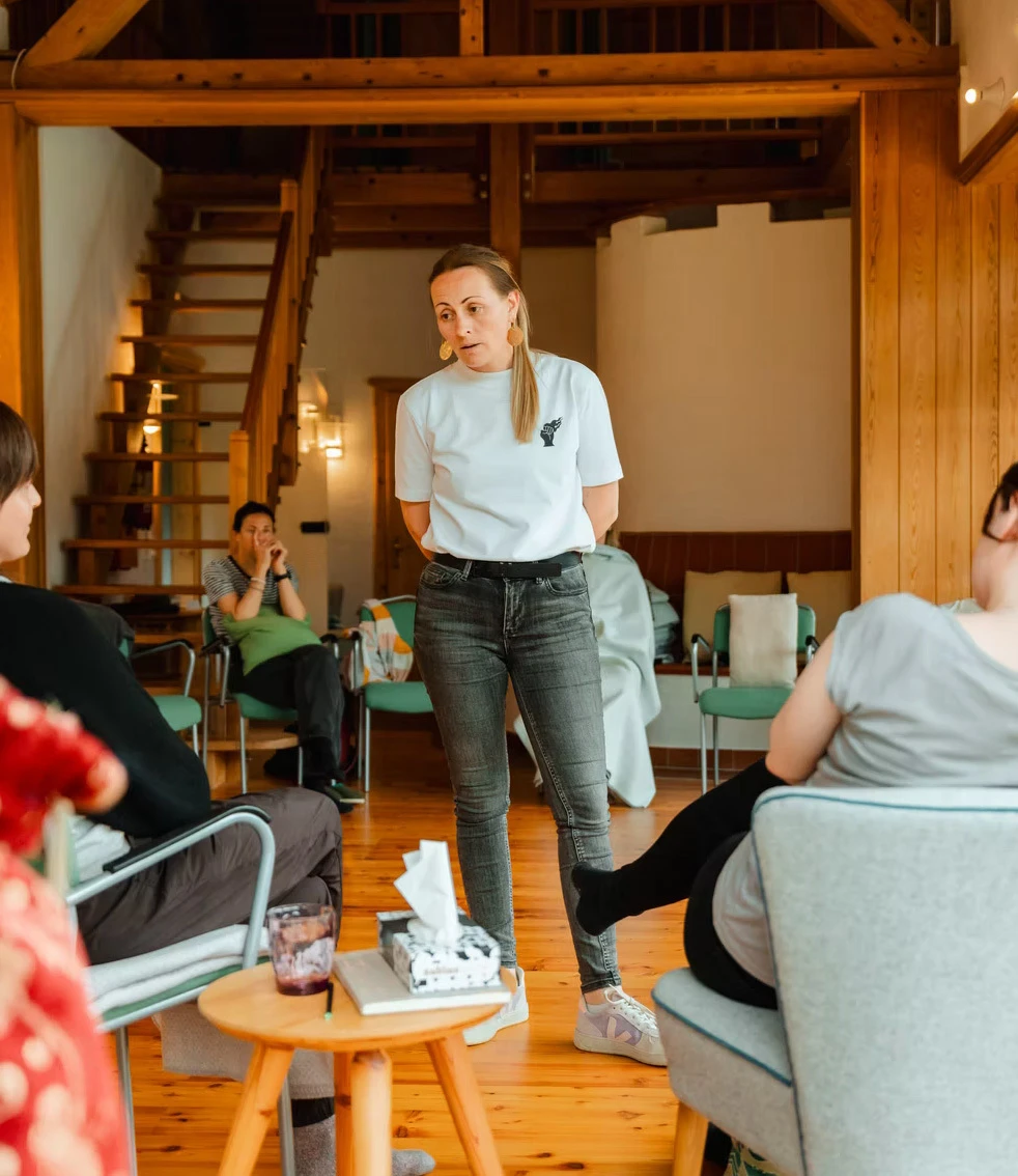 Person hält Vortrag vor Gruppe in einem warmen Holzzimmer während eines Workshops.