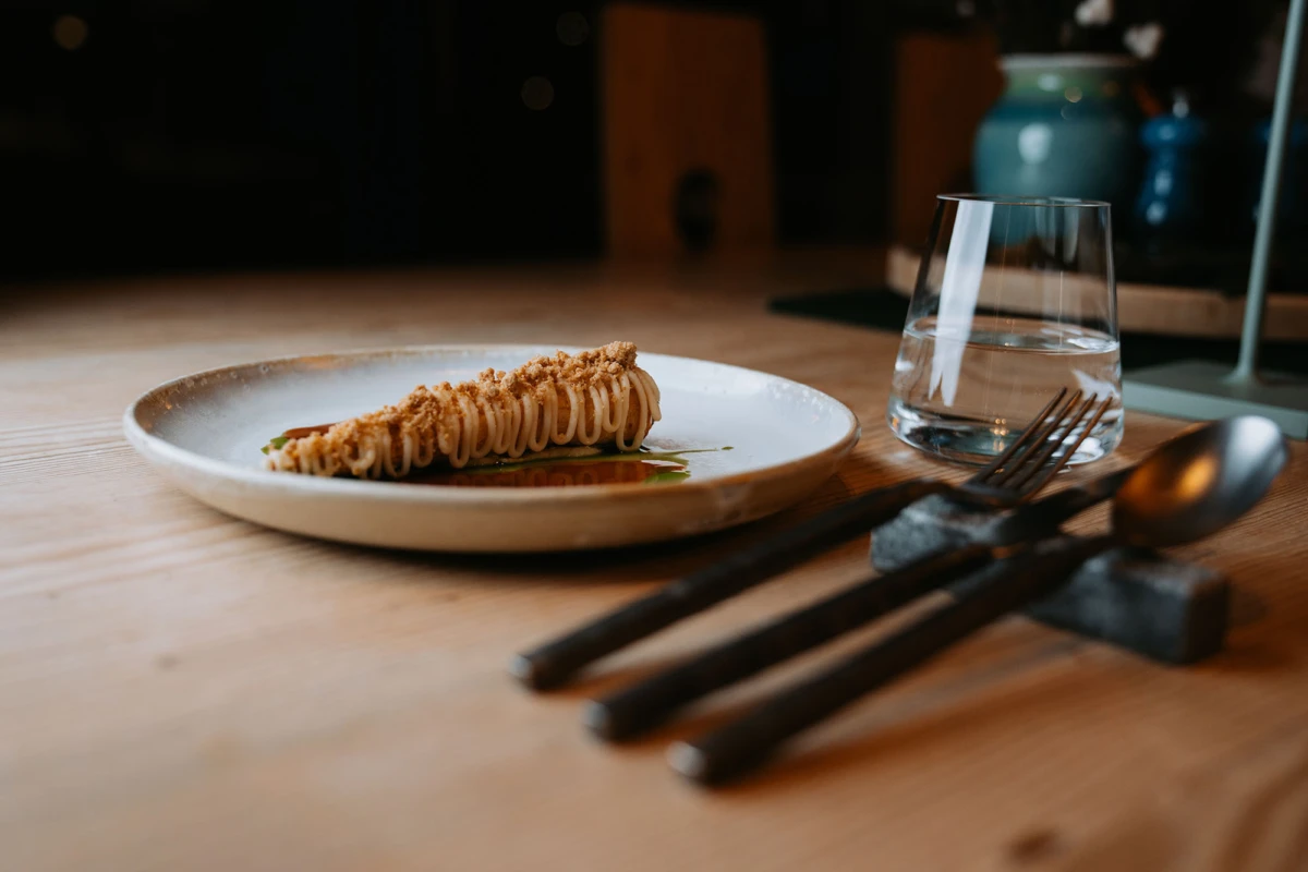 Heller Teller mit Blätterteigrolle in Sauce; Glas Wasser, Besteck auf Holztisch in rustikaler Restaurantatmosphäre.