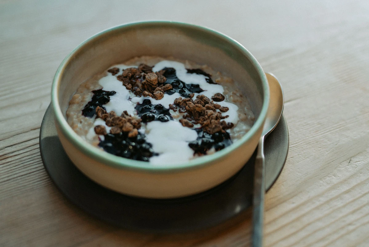 Schüssel Haferbrei mit Joghurt, Heidelbeeren und Knuspermüsli auf dunklem Teller, Holzoberfläche.