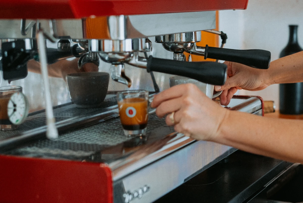 Espressomaschine im Café, Barista bedient zwei Portafiltern und füllt Espresso in ein Glas.