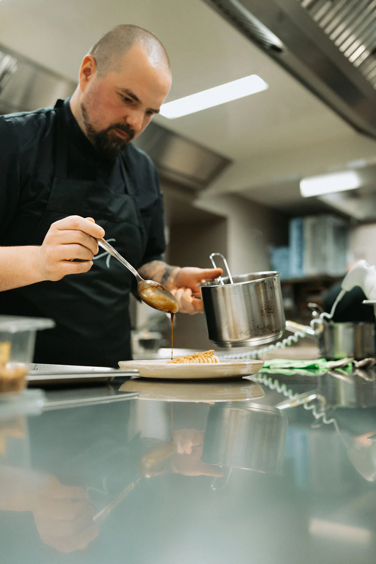 Koch in Restaurantküche gießt Soße über ein Gericht.