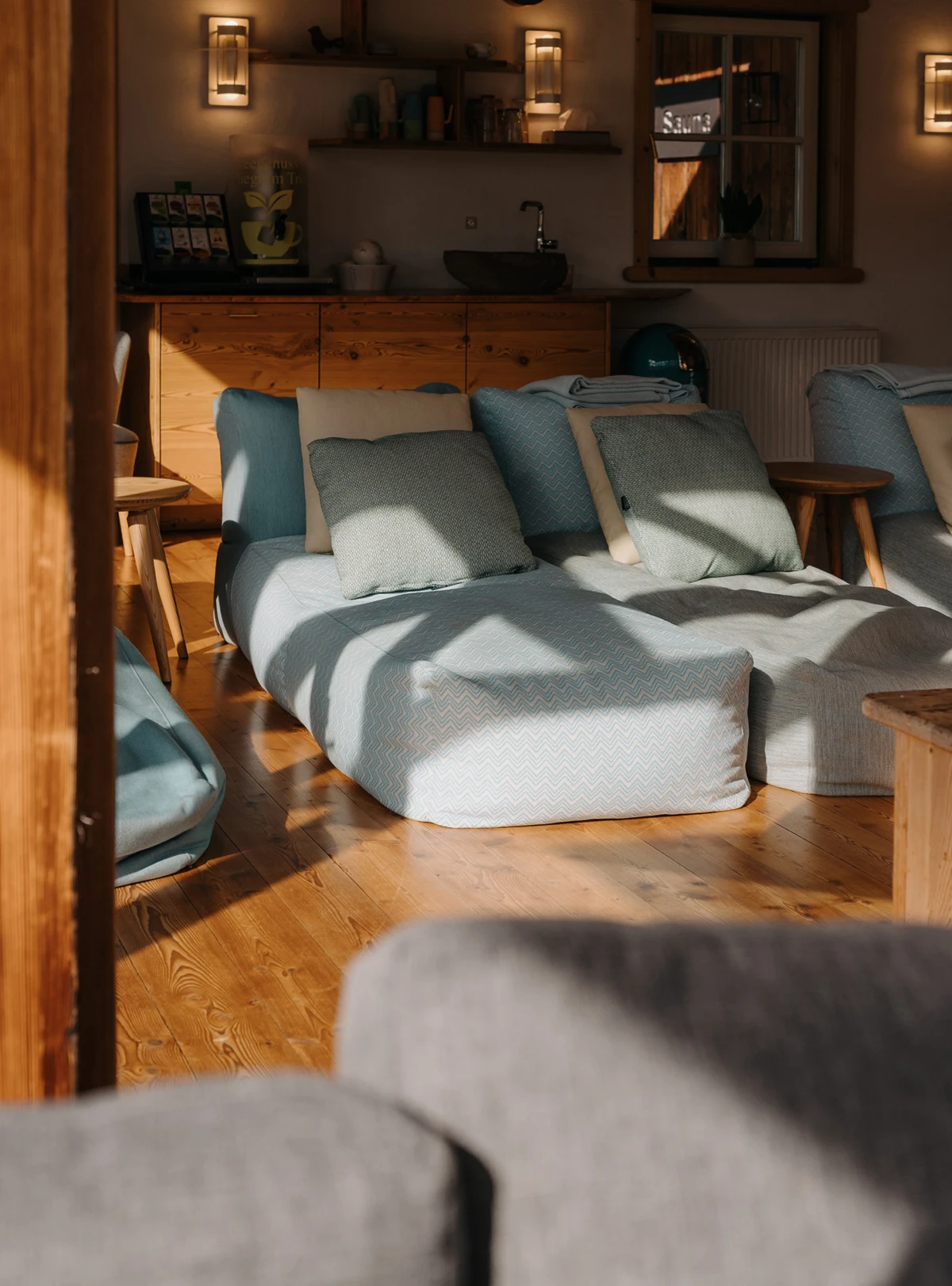 Gemütliche Sitzecke mit hellblauem Sofa und Kissen in einer Holzhütte; Küchenbereich mit Spüle im Hintergrund, warmes Licht.