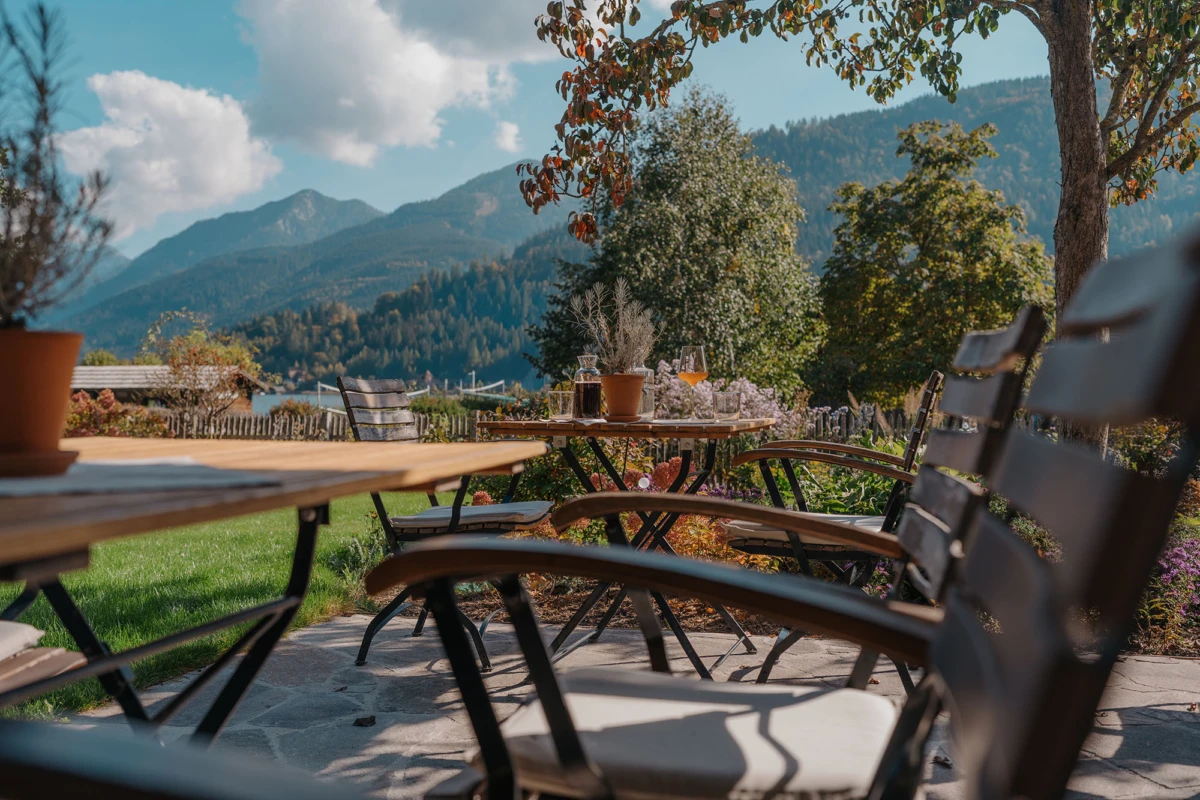 Holztische und Stühle im Freien auf Terrasse; Berglandschaft im Hintergrund.