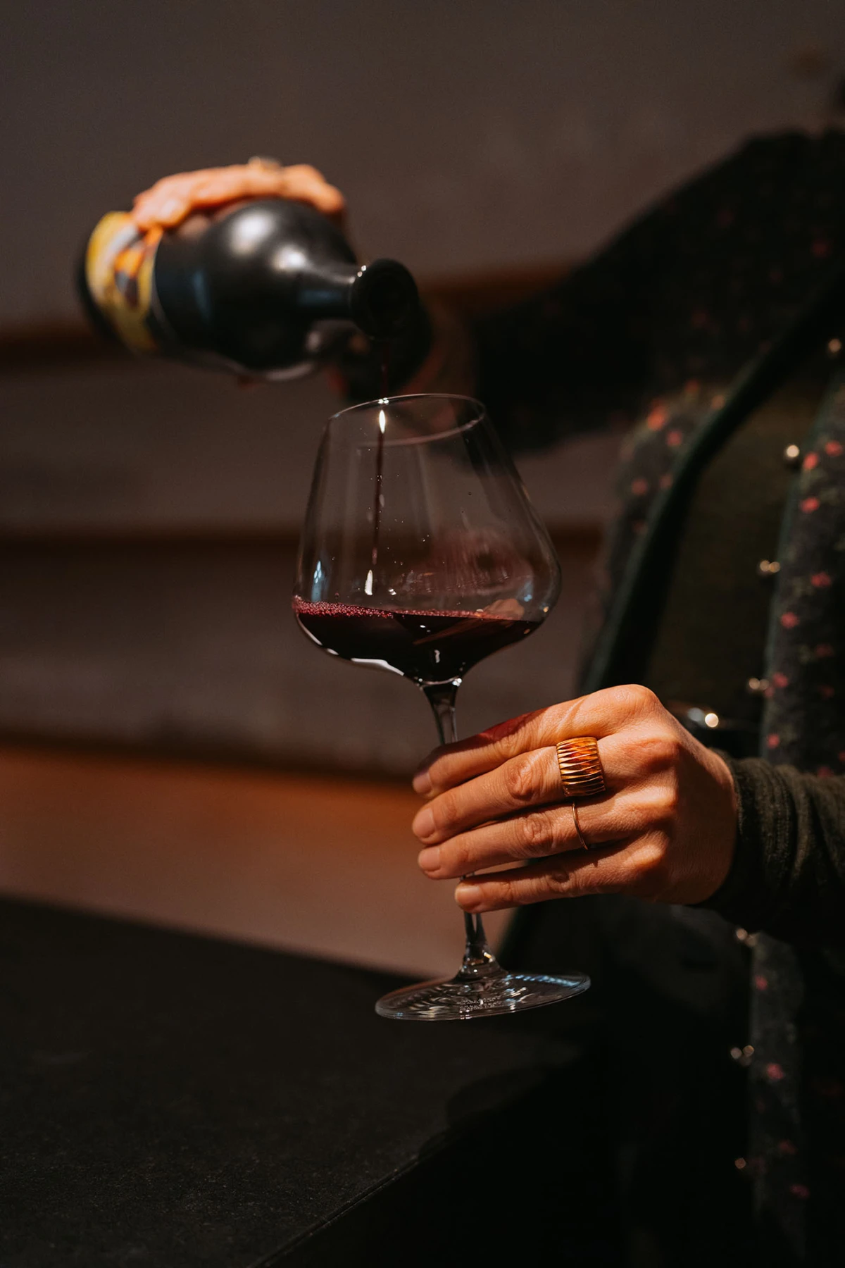 Person gießt Rotwein aus der Flasche in Weinglas auf Bar-Theke.