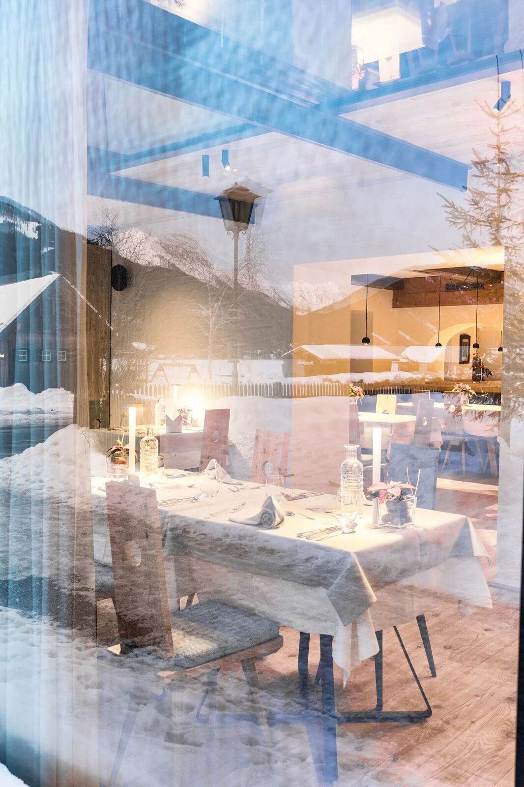 Festlich gedeckter Esstisch im winterlichen Restaurant, Blick durch Glasfenster auf verschneite Außenlandschaft.
