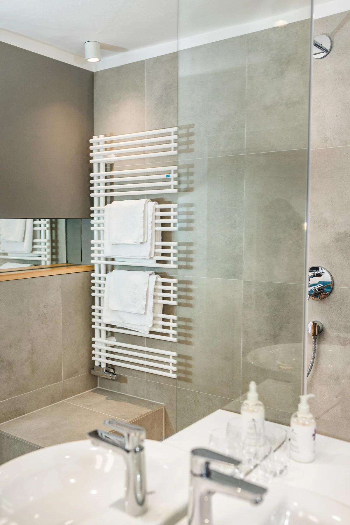Modernes Badezimmer mit weißem Handtuchheizkörper, gehängten Handtüchern, Waschbecken und Dusche.