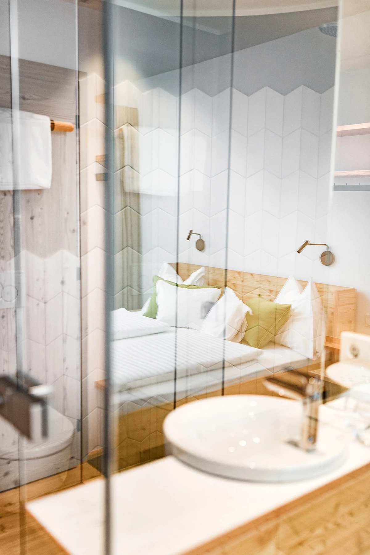 Waschbecken im Vordergrund, Glaswand; Schlafzimmer mit Bett und Kissen, moderne Einrichtung.