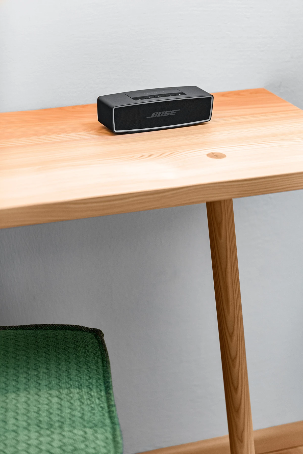 Bose-Lautsprecher steht auf Holztisch vor heller Wand.