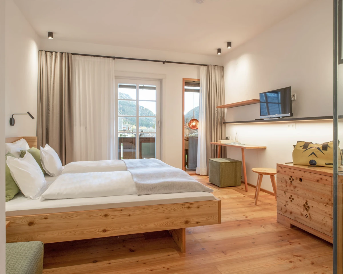 Hotelzimmer mit Holzbettgestellen, weiße Bettwäsche, Schreibtisch, TV, Balkon mit Bergblick.