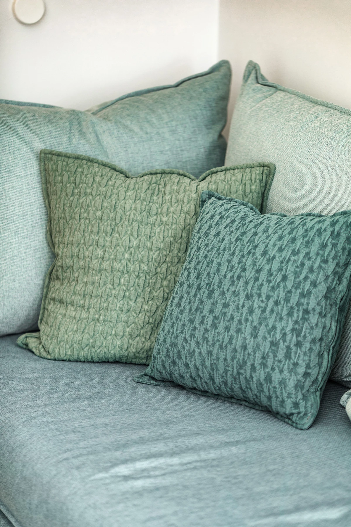 Sofa mit drei gemusterten Kissen in Grün- und Blautönen in heller Wohnzimmerecke
