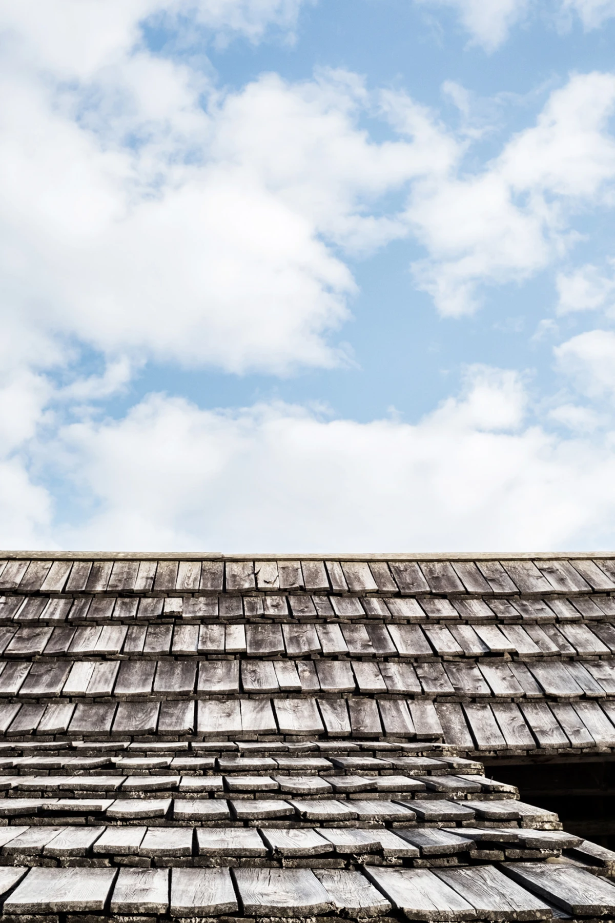 Verwittertes Holzschindeldach unter blauem Himmel mit Wolken.