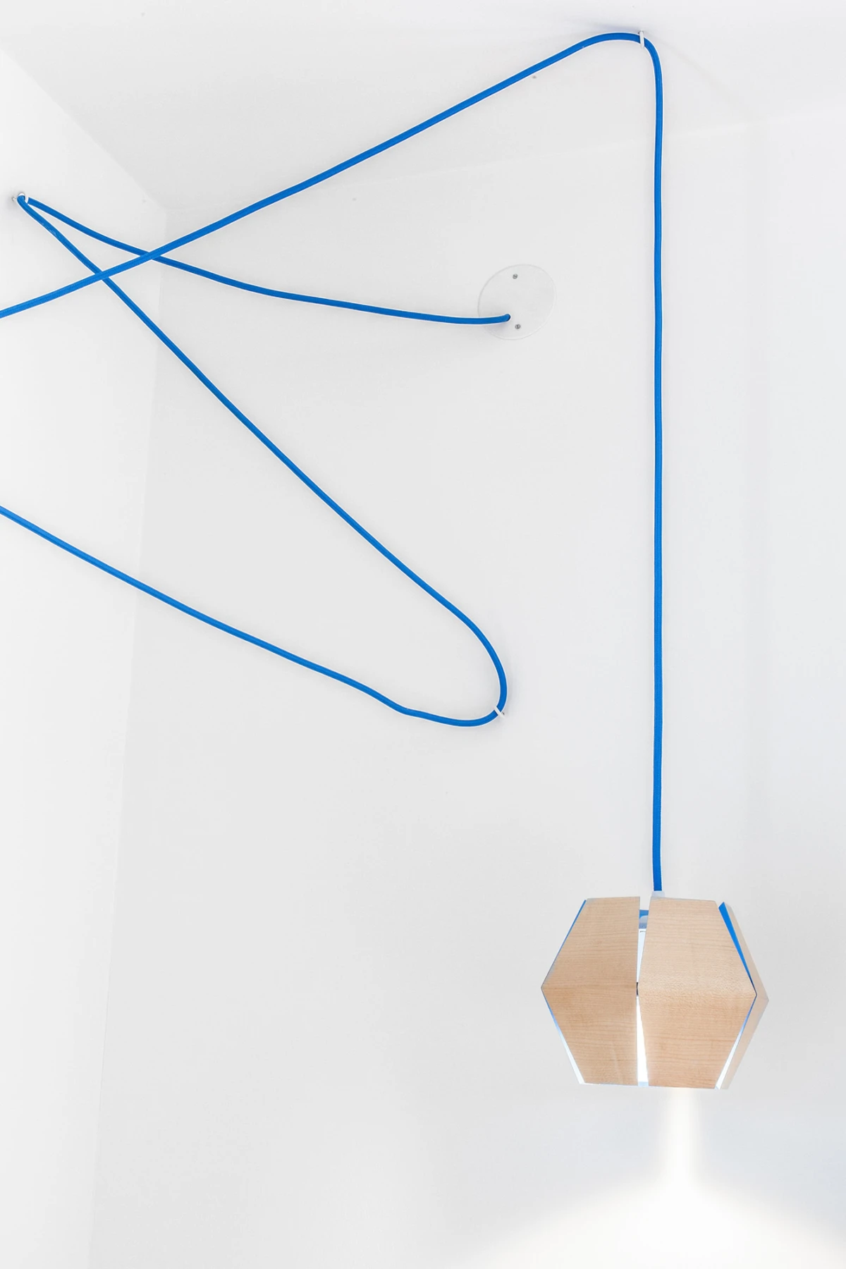 Pendelleuchte mit hexagonaler Holzlampe und blauem Kabel, hängt von weißer Decke herab.